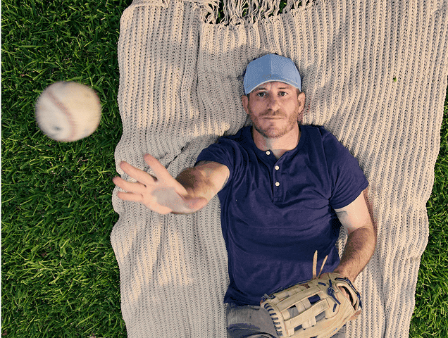 Man with narcolepsy type 1 laying down on a blanket outdoors and throwing a baseball into the air