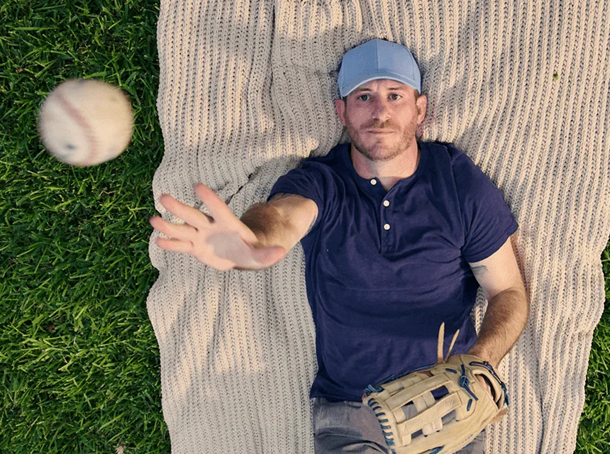 Man with narcolepsy type 1 laying down on a blanket outdoors and throwing a baseball into the air