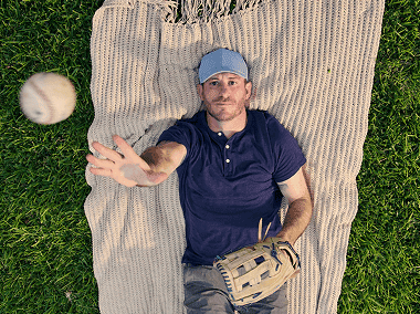Man with narcolepsy type 1 laying down on a blanket outdoors and throwing a baseball into the air
