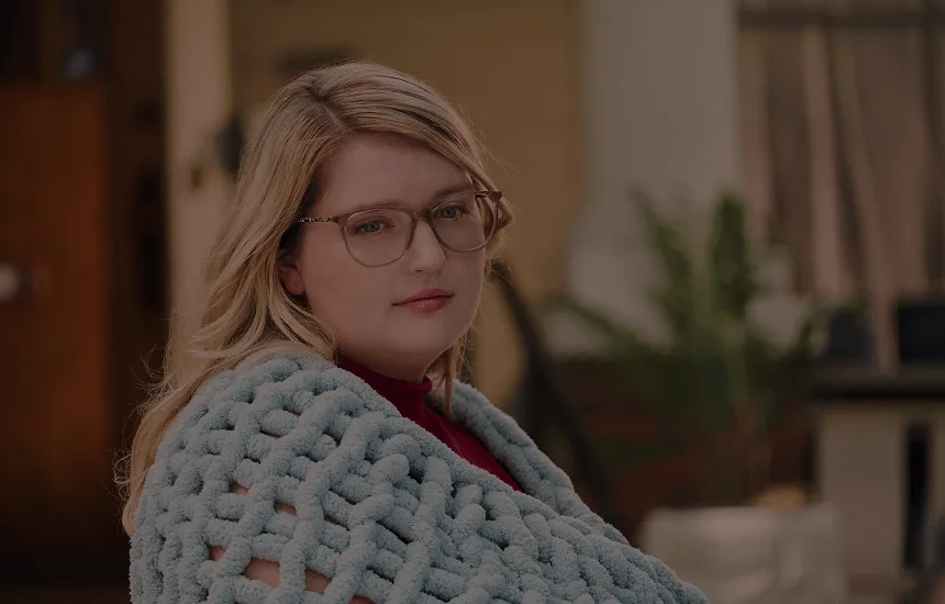 Woman with narcolepsy type 1 posing outdoors while wrapped in a knitted blanket